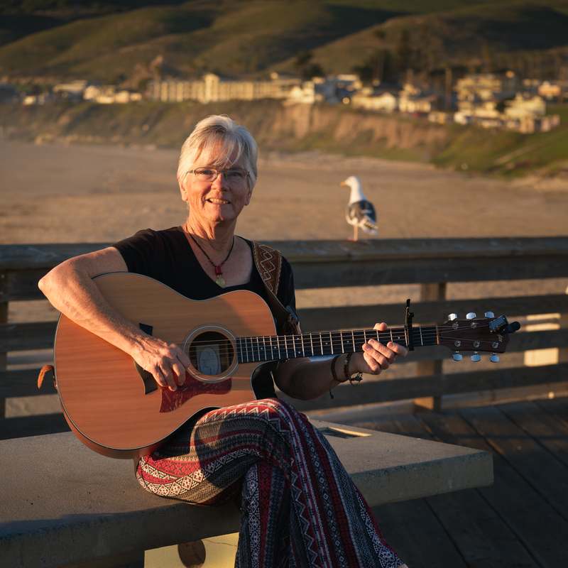 Joelyn Lutz seated with her guitar on the Pismo Beach pier at golden hour